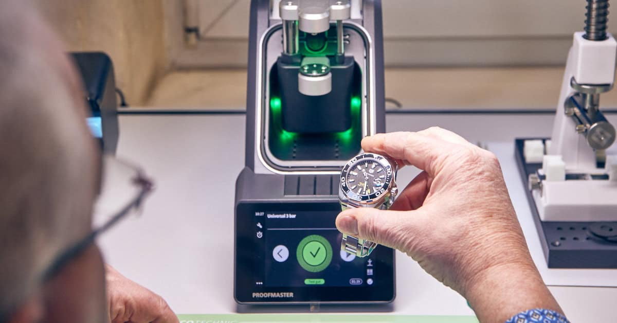 Mitarbeiter hält Uhr in der Hand, im Hintergrund das Prüfgerät