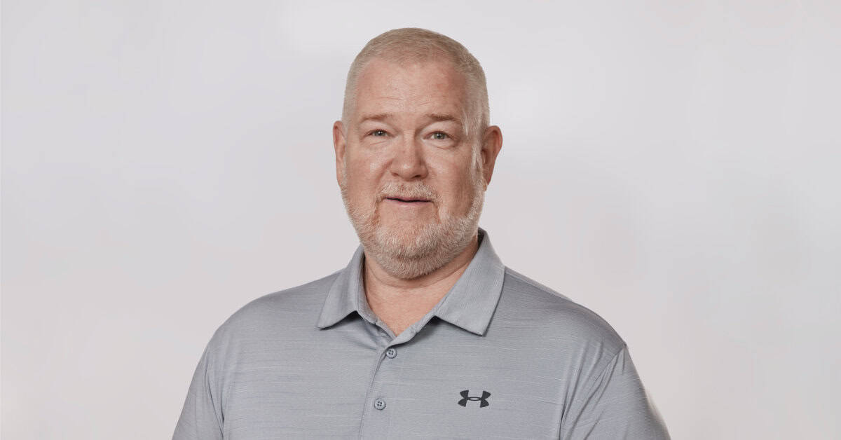 Porträtfoto von Herrn Brewer. Der Mann trägt Dreitagebaart, ein legeres Polohemd und schaut freundlich in die Kamera; neutraler heller Fotohintergrund.